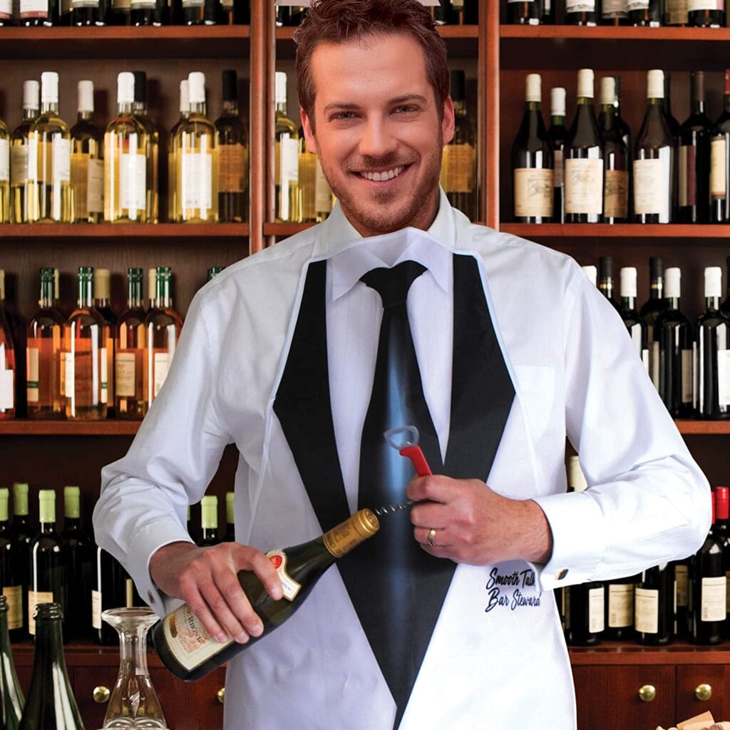 Image shows the bar steward side of the apron being worn. A man is opening a bottle of wine using the supplied bottle opener. Wine bottles in wooden cubes are in the background.