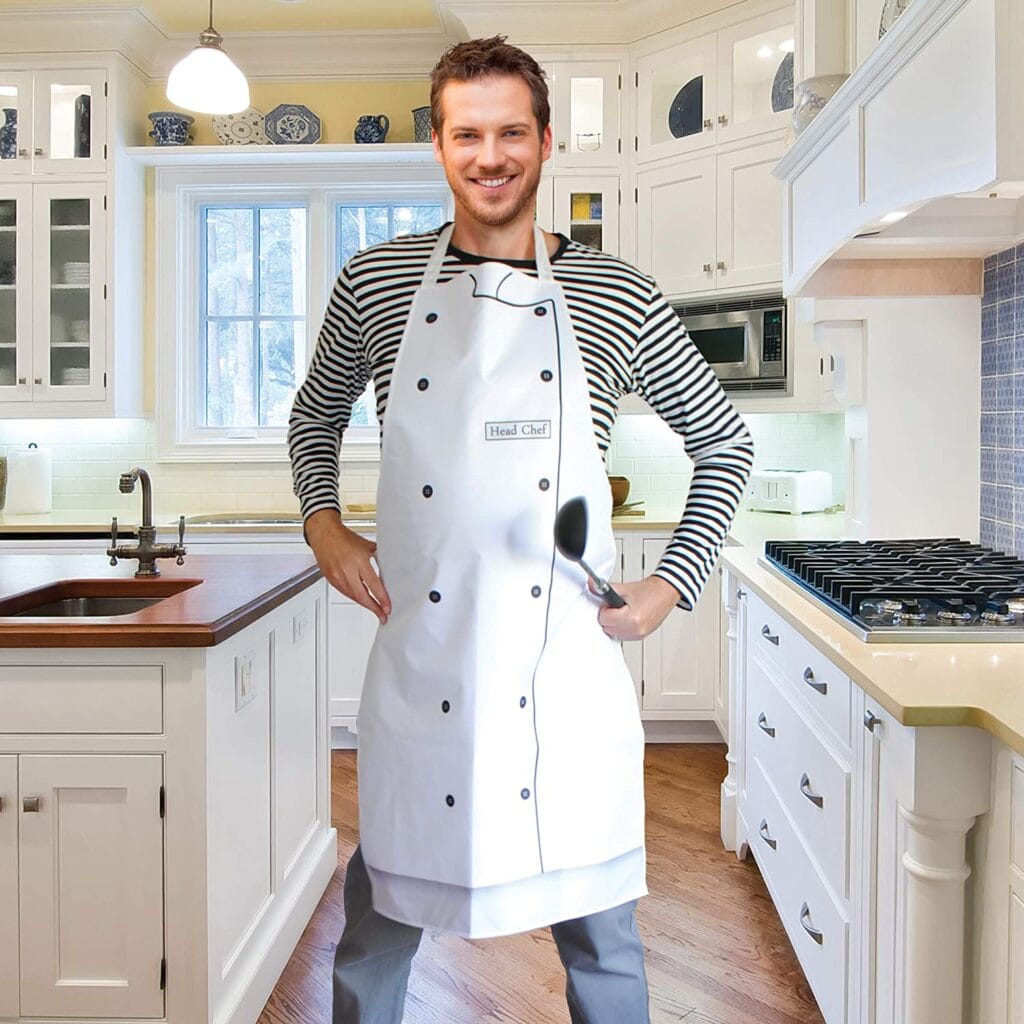 Image shows the apron being worn as the chef by a man with his hands on his hips. The background features a kitchen.