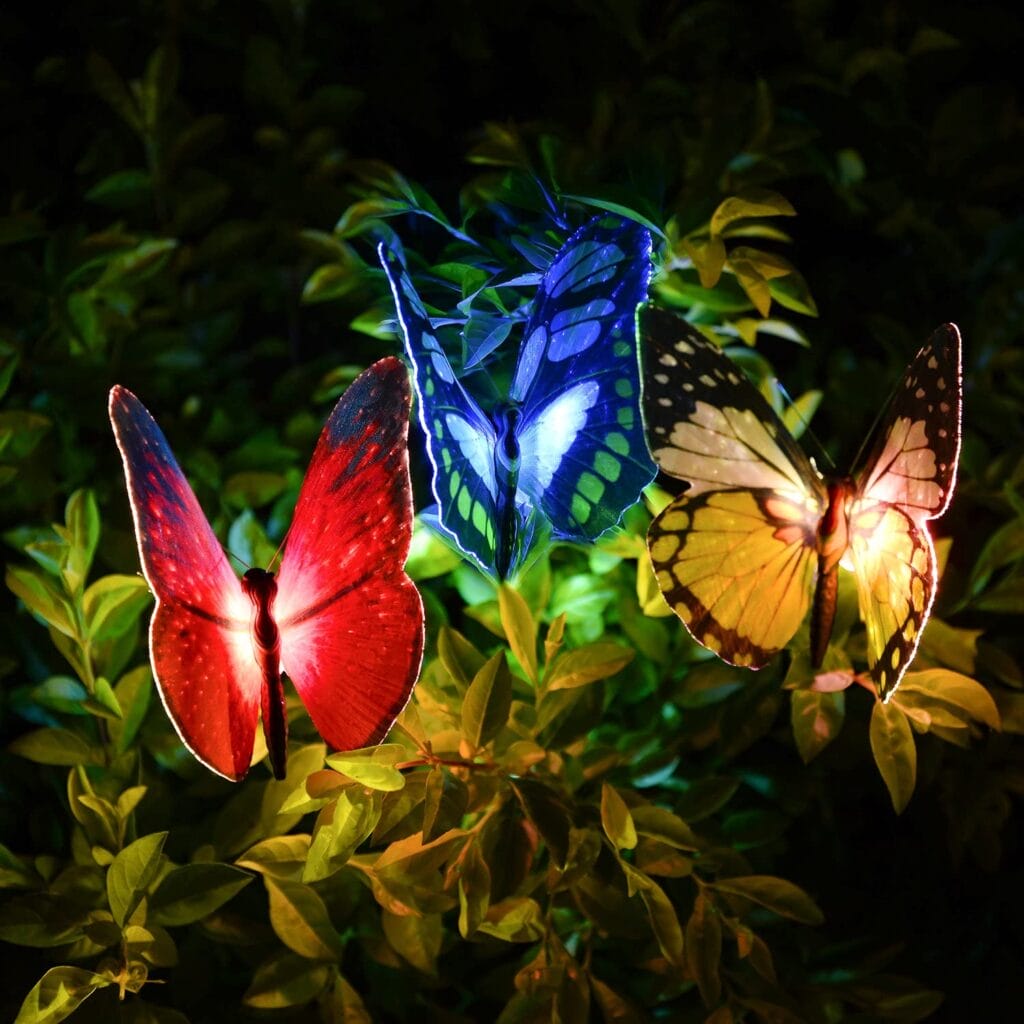 Image shows 3 butterfly lights lit up in a bush.