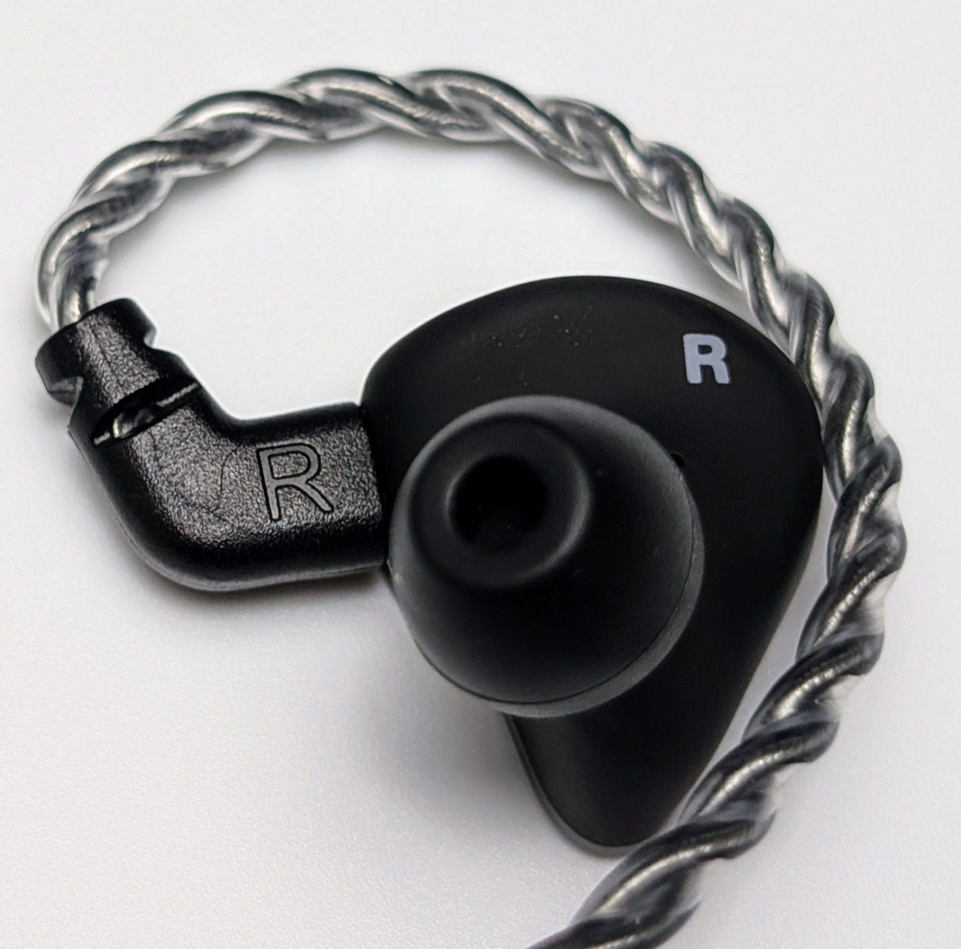 Agasound AgaOne IEMs Image of the right side of an Agasound AgaOne IEM with its cable attached. The IEM has a black housing with the letter 'R' indicating the right earpiece. The earpiece nozzle is visible, designed for inserting ear tips. The cable is braided with a silver and black pattern, connecting to the IEM via a black connector.