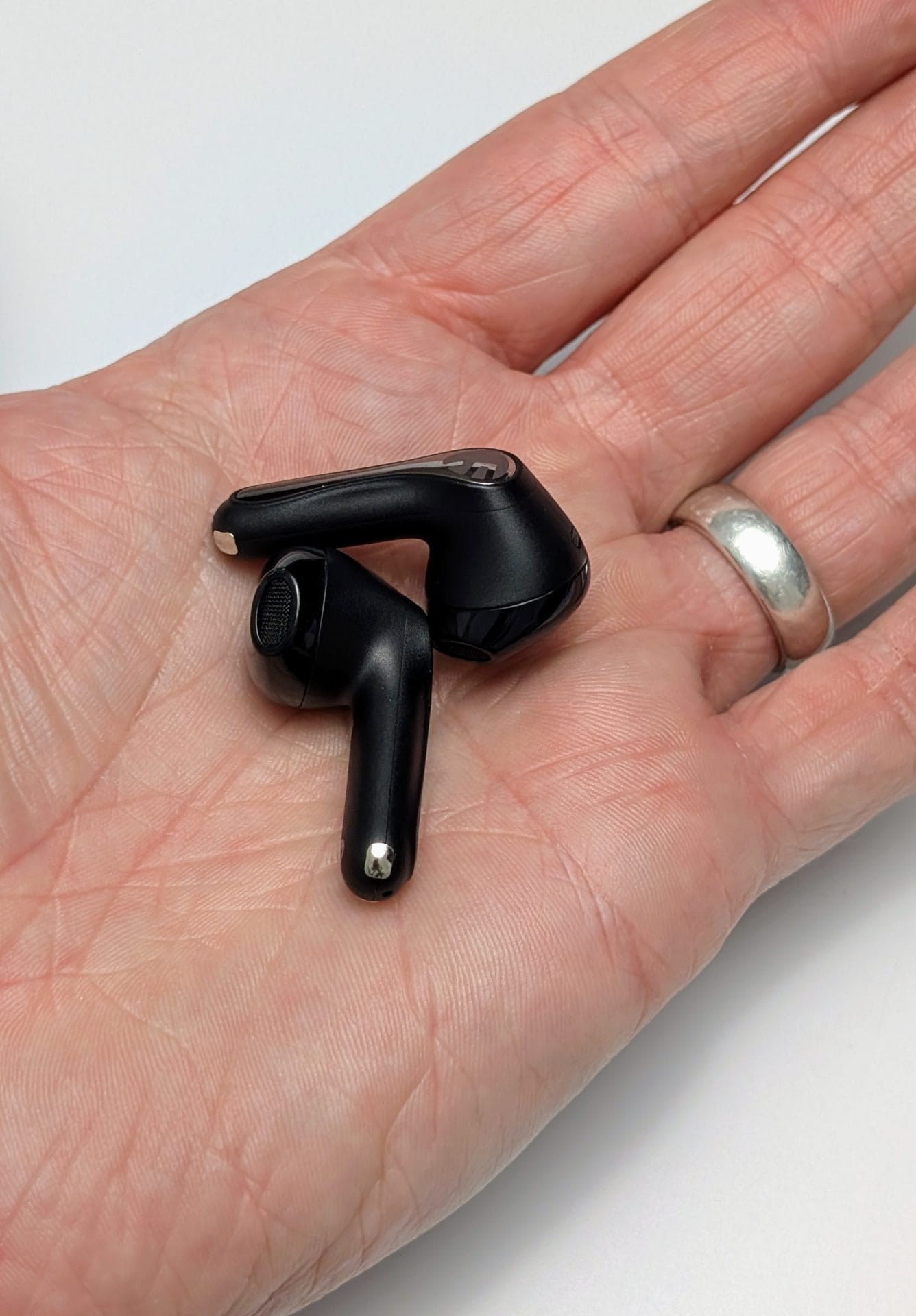 SoundPEATS Air5 Earbuds Image of a hand holding two SoundPEATS Air5 wireless earbuds. The earbuds are black with a sleek design, featuring a metallic accent on the top part. The hand is open, palm up, with the earbuds resting on it. The person wearing the hand also has a silver ring on their ring finger.