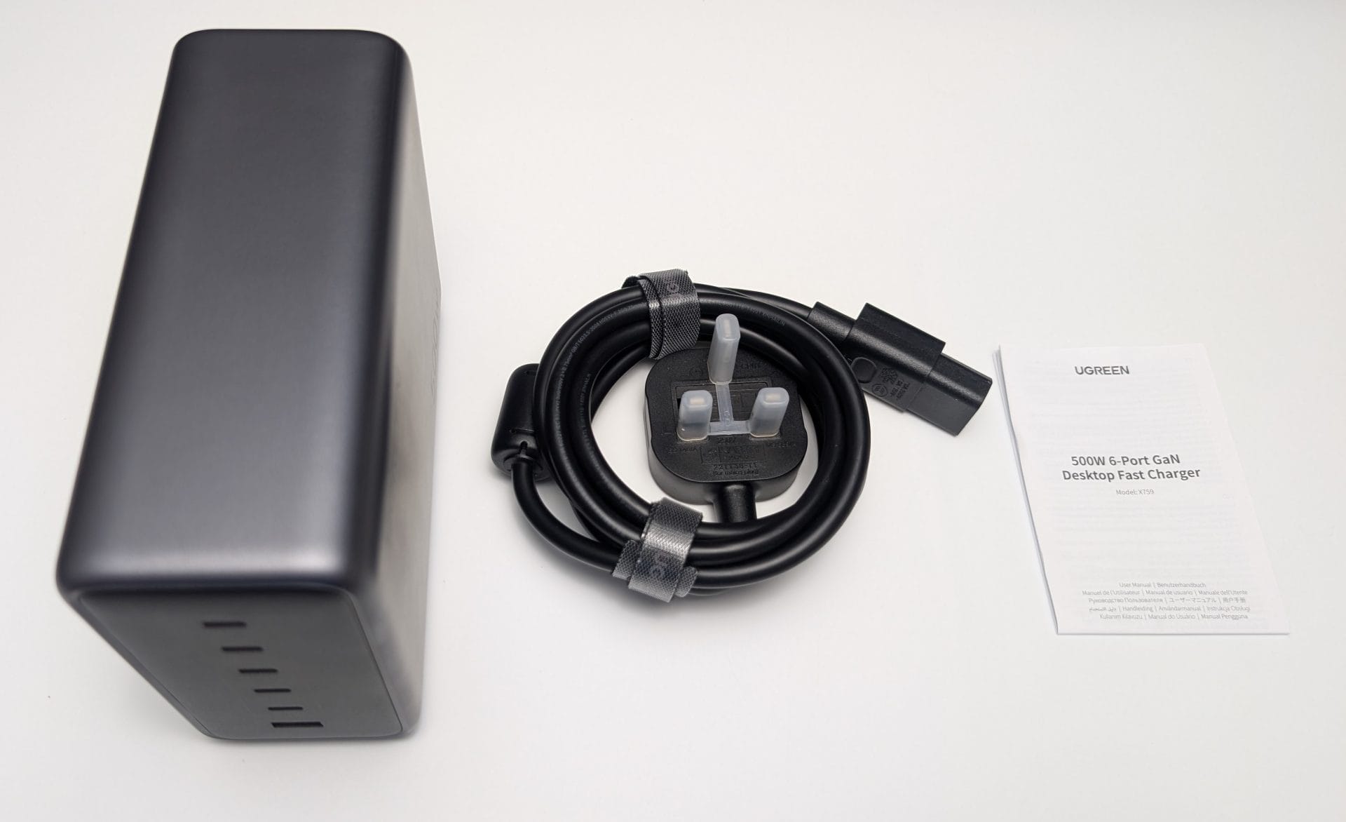 UGREEN Nexode 500W Charger The unboxed UGREEN Nexode 500W 6-Port GaN Desktop Charger (Model: 15796) in grey, placed on a white surface. It features multiple ports on one side. Next to it is a coiled 2-metre black power cord with a UK plug, secured with a strap. A folded instruction manual labelled "UGREEN 500W 6-Port GaN Desktop Charger" is also included. The setup is photographed on 31 May 2025 at 09:57 AM BST.
