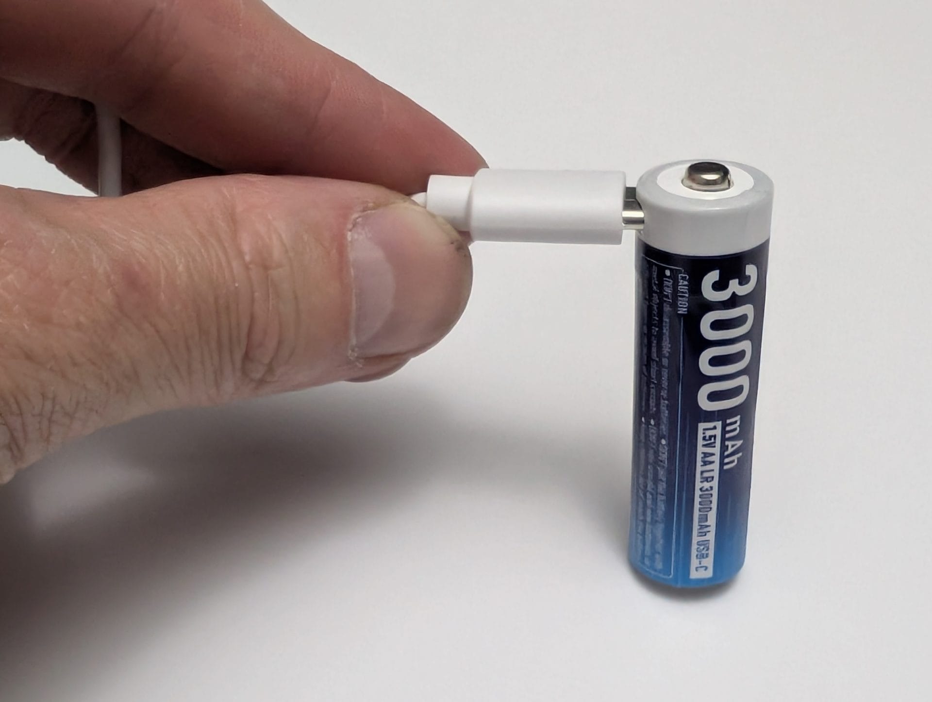 A hand inserting four XTAR AA batteries into the battery compartment of a black smart lock mounted on a white door. The background shows a blurred indoor setting with a sofa and furniture. The lock is positioned next to a traditional door latch.