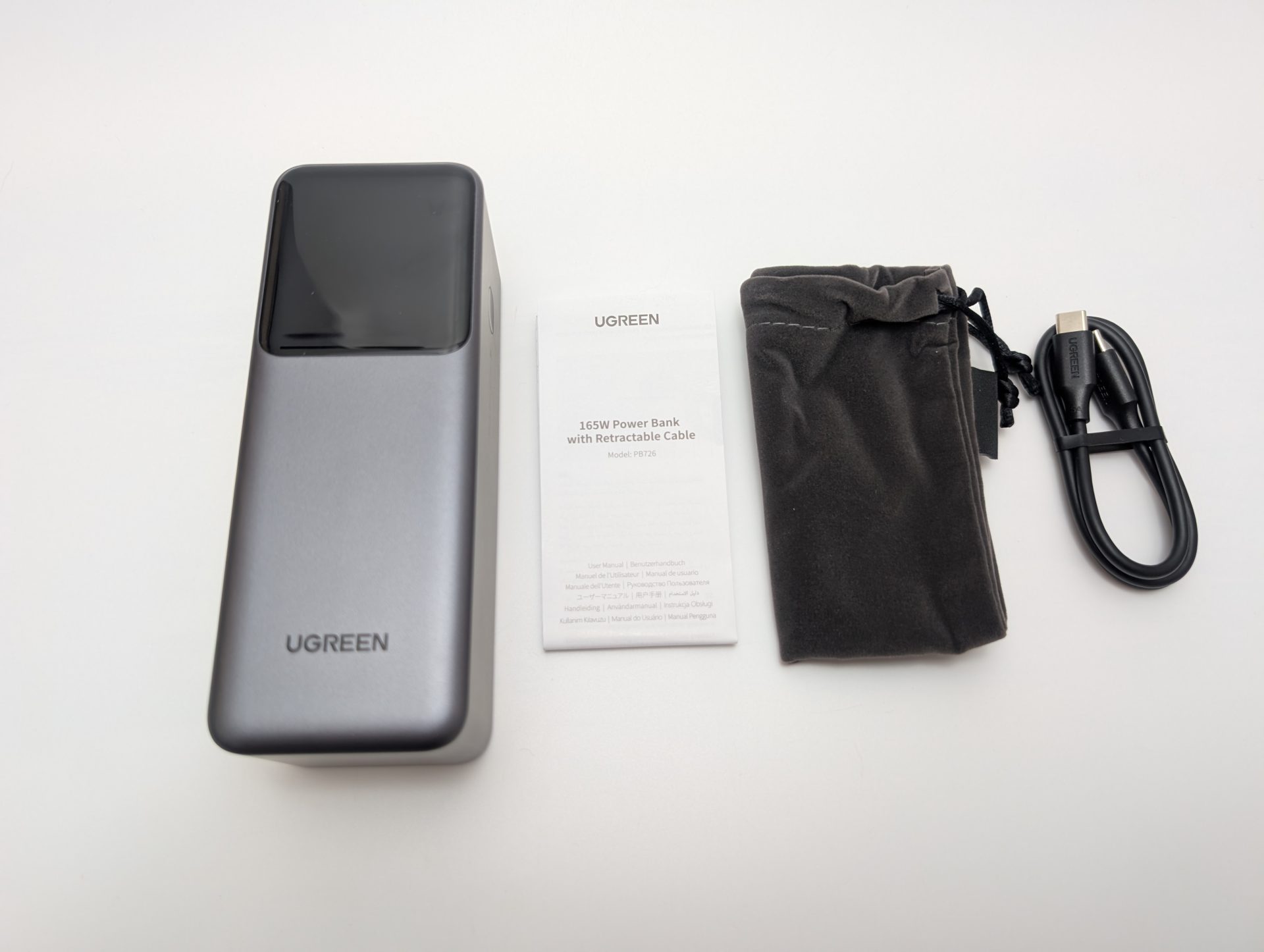 UGREEN Nexode Power Bank 20000mAh 165W with Retractable USB-C Cable UGREEN Nexode 20000mAh 165W Power Bank with Retractable USB-C Cable unboxed. The image shows the sleek silver and black power bank, a user manual, a gray velvet pouch, and an additional black USB-C cable. The power bank features the UGREEN logo and a glossy top panel.