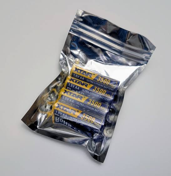 A sealed, metallic zip-lock bag containing four XTAR Ultra3500D AA lithium non-rechargeable batteries. Each battery is yellow with blue and white text, labeled "XTAR Ultra Lithium Battery," "1.5V AA," and "3500 mAh." The packaging is placed on a plain, light grey surface.