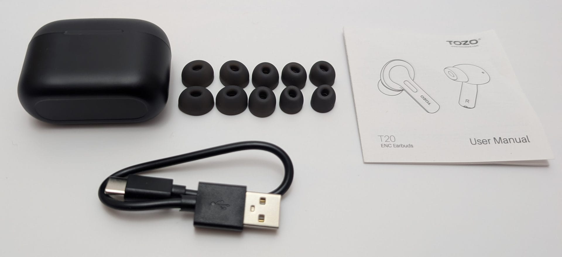 TOZO T20 Wireless Earbuds Image of TOZO T20 earbuds accessories, including a black charging case, a USB-A to USB-C charging cable, multiple pairs of black ear tips in various sizes, and a user manual with diagrams of the earbuds labeled "L" and "R".