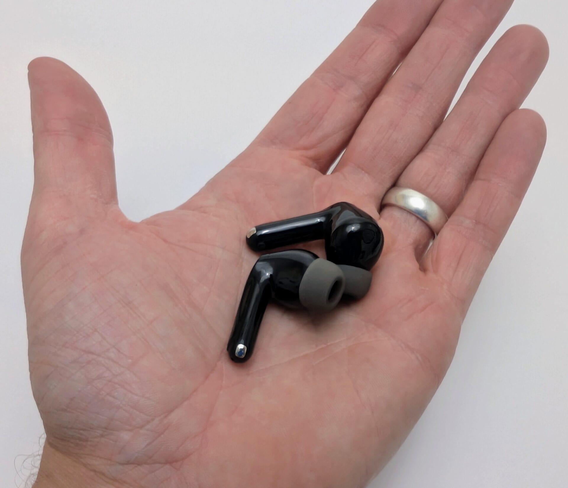 Alt text: Image of a hand holding two black SoundPEATS Air5 Pro earbuds with gray ear tips, showcasing their compact design. The hand is adorned with a silver ring, and the background is a plain white surface.