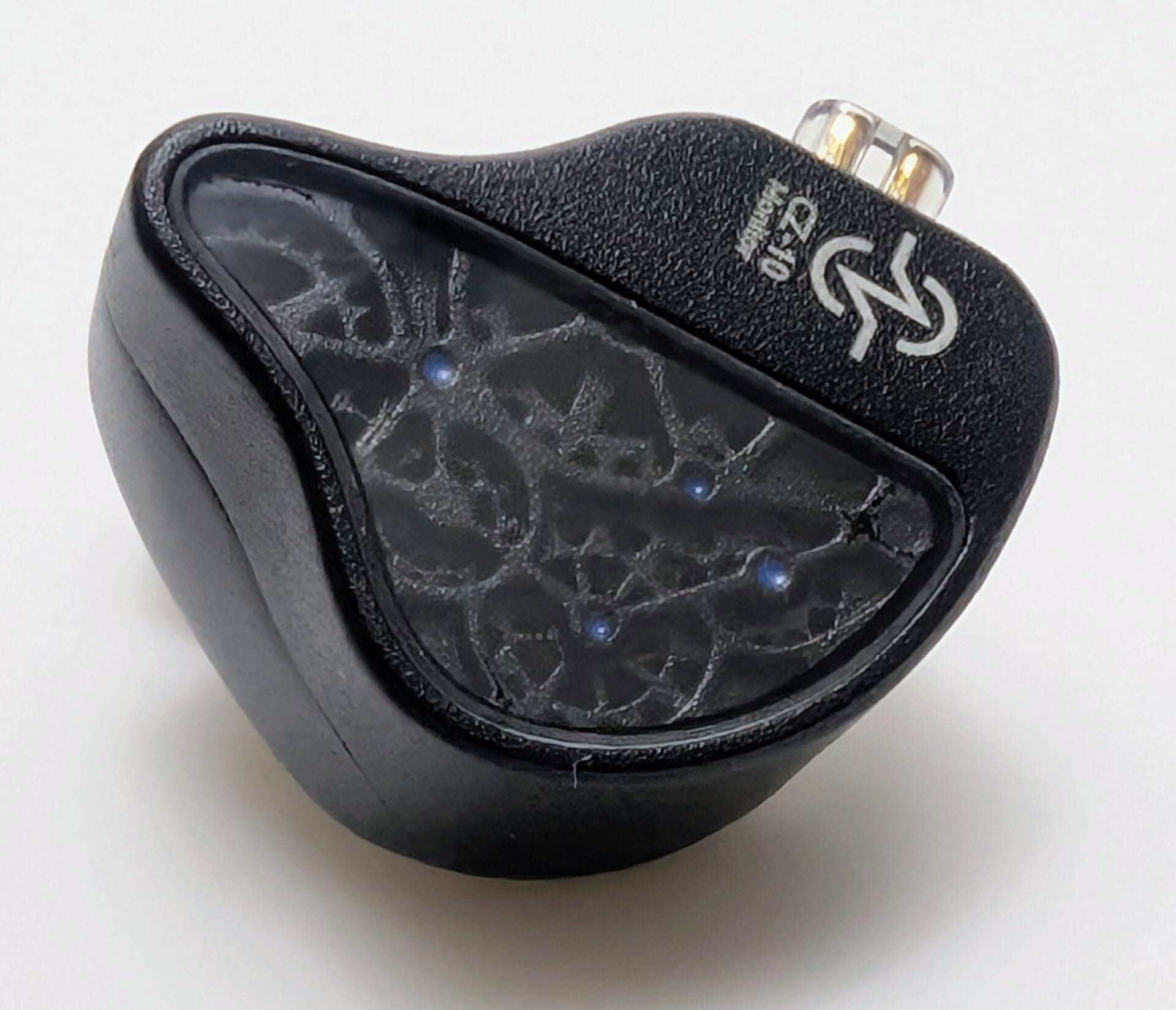 CCZ TianGong CZ10 A high-detail macro shot of a single CCZ TianGong CZ10 in-ear monitor resting on a white surface. The image emphasizes the textured black finish of the shell and the detailed, dark-toned gear patterns visible through the transparent faceplate. The silver "CZ-10 Monitor" branding is clearly visible at the top.