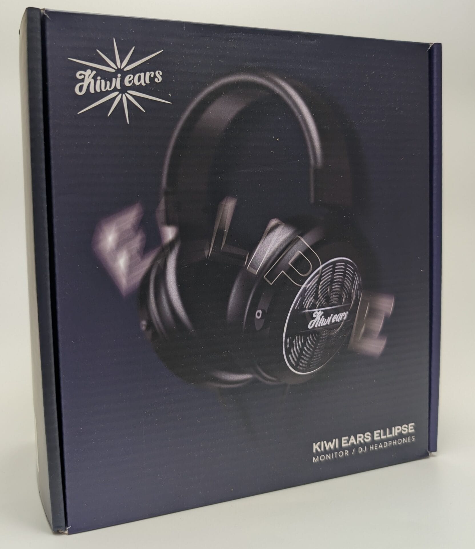 Dark navy blue retail box for Kiwi Ears Ellipse over-ear DJ/monitor headphones. Front shows angled view of black headphones with perforated metallic ear cups, white cursive “Kiwi Ears” logo, starburst graphic, and text “KIWI EARS ELLIPSE – MONITOR / DJ HEADPHONES”. Sleek, premium design photographed straight-on.