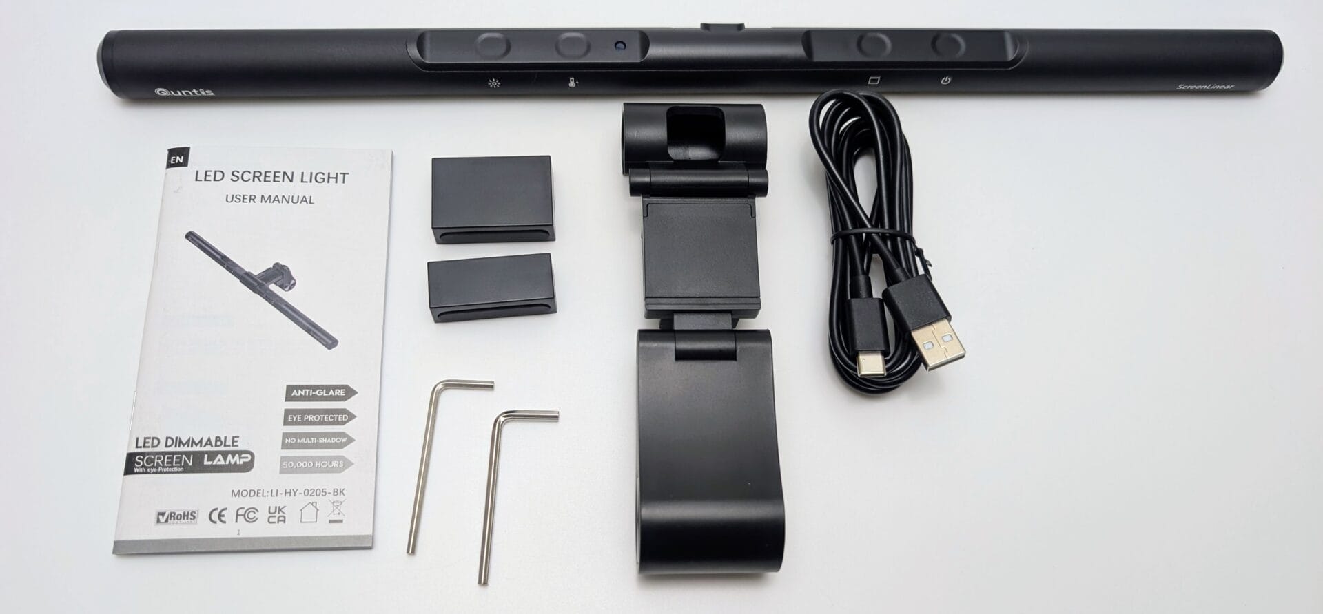 Unboxed Quntis Monitor Light Bar kit including the black touch-control LED light bar, USB-C cable, adjustable monitor clip, counterweights, two hex keys, and user manual, all laid out on a white surface.