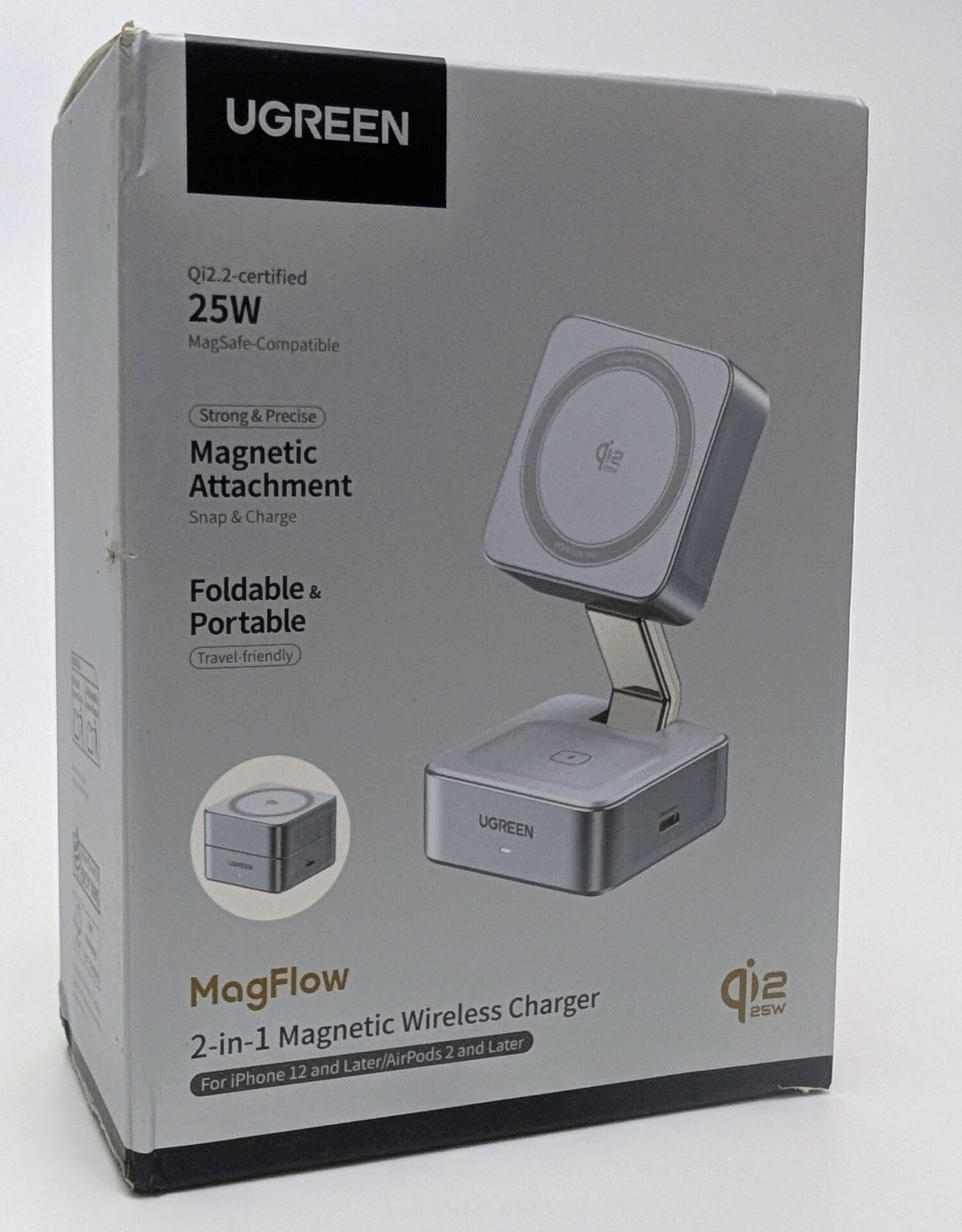 UGREEN MagFlow 2-in-1 Magnetic Wireless Charger 25W The retail packaging box for the UGREEN MagFlow 2-in-1 Magnetic Wireless Charger, a Qi2-certified 25W foldable MagSafe-compatible stand. The sleek silver-gray box displays the product in its upright charging position with a metallic folding arm supporting a square magnetic pad showing the Qi logo. Bold text highlights include "Qi2.2-certified 25W", "MagSafe-Compatible", "Strong & Precise Magnetic Attachment", "Snap & Charge", "Foldable & Portable", and "Travel-friendly". A small inset shows the charger compactly folded. Branding reads "MagFlow 2-in-1 Magnetic Wireless Charger" for iPhone 12 and later / AirPods 2 and later, with the UGREEN logo at the top. The box has minor wear at the edges.