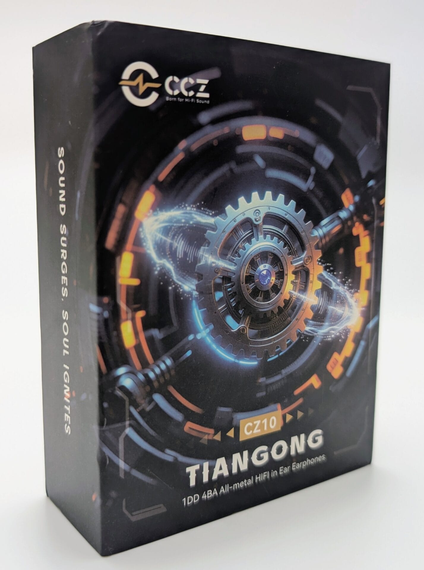 CCZ TianGong CZ10 A black product box for the CCZ TianGong CZ10 in-ear monitors. The front features futuristic, mechanical gear graphics with glowing blue and orange lighting effects. The brand logo "CCZ" is at the top, and the text at the bottom identifies them as "1DD 4BA All-metal HiFi In-Ear Earphones." The side of the box reads, "SOUND SURGES, SOUL IGNITES."
