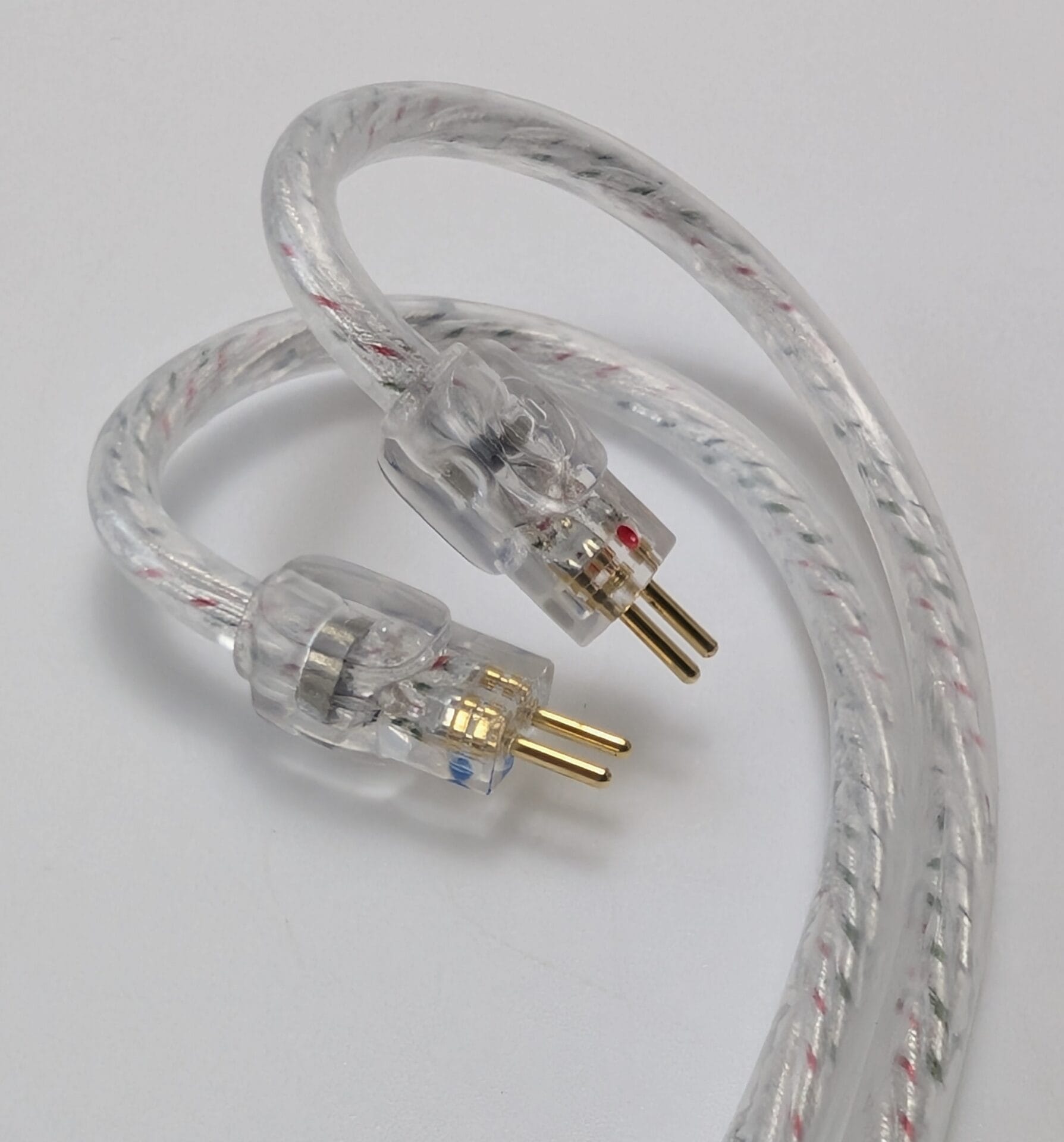 Close-up of the detachable silver braided cable for the Kiwi Ears Belle in-ear monitors. The transparent cable features red and green strands woven throughout and is shown with its two 0.78mm two-pin connectors (one marked with a red dot, the other with a blue dot) with gold-plated pins.