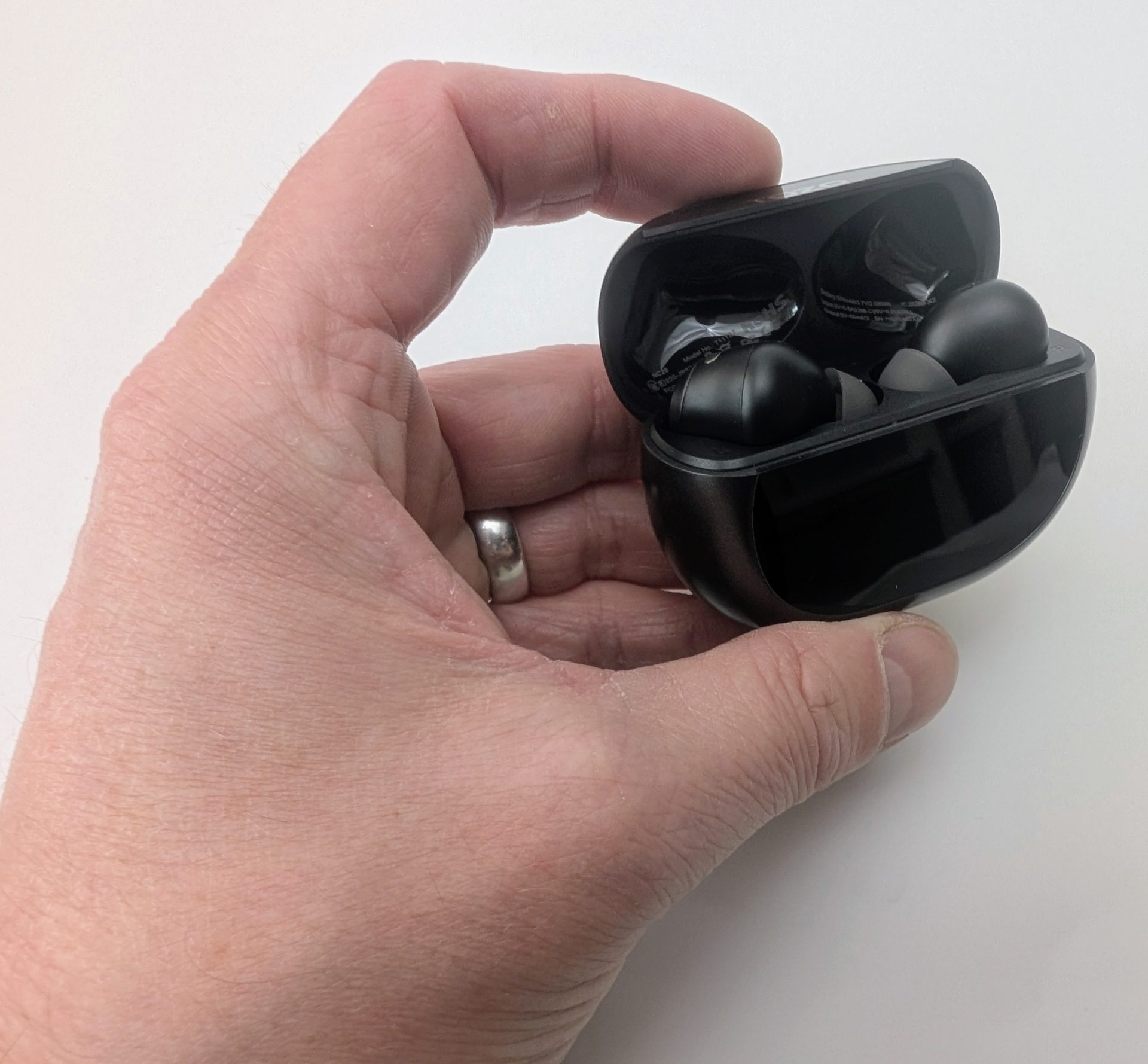 TOZO NC20 Earbuds Human hand holding an open black TOZO NC20 charging case, revealing the two black wireless earbuds stored inside. The glossy case is held in the palm, with a silver ring visible on the person's ring finger.