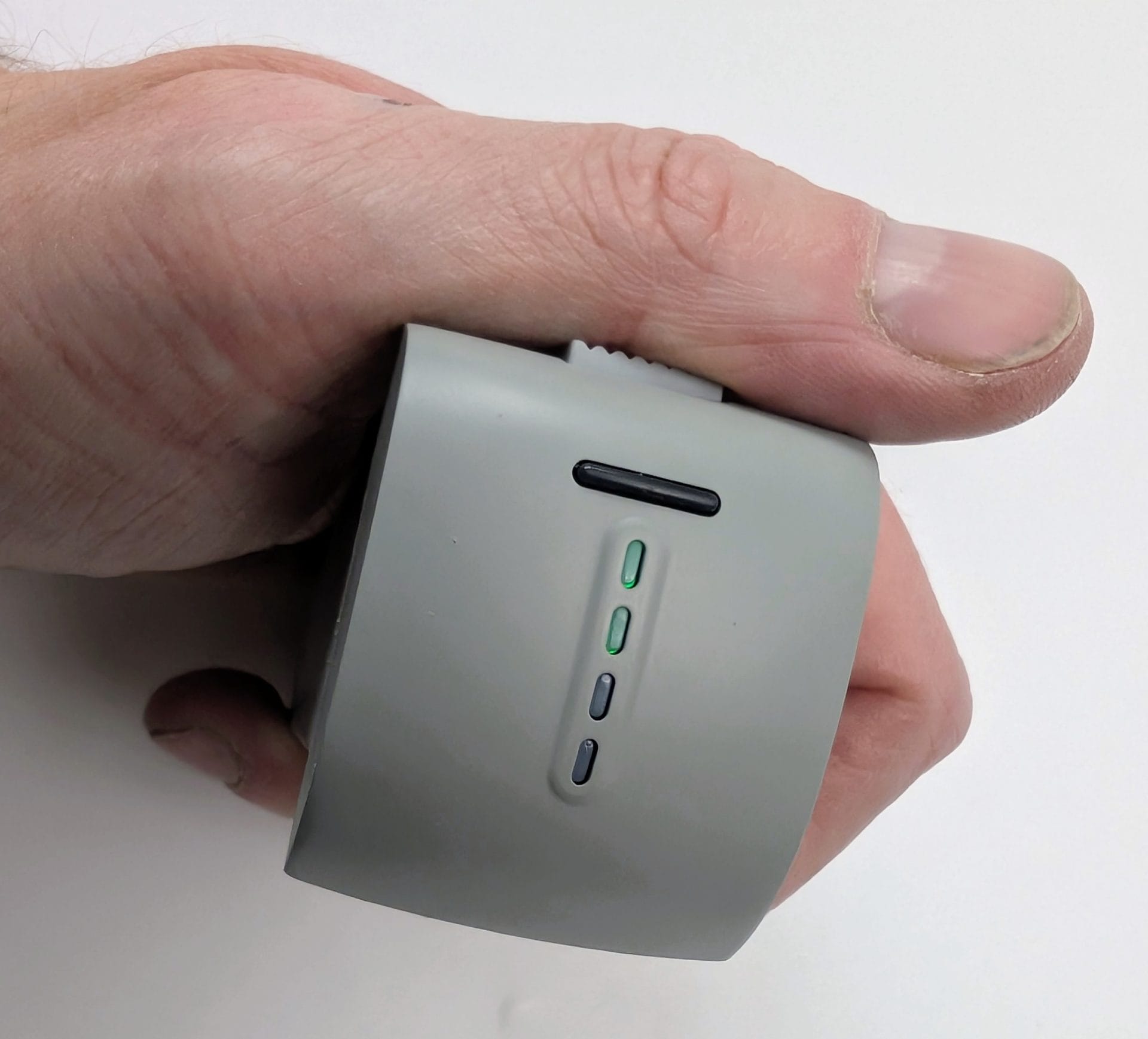 A hand holding the gray Ruko F11PRO 2 Plus drone battery, showing the side with a USB-C charging port and four LED battery level indicators (one green light illuminated).