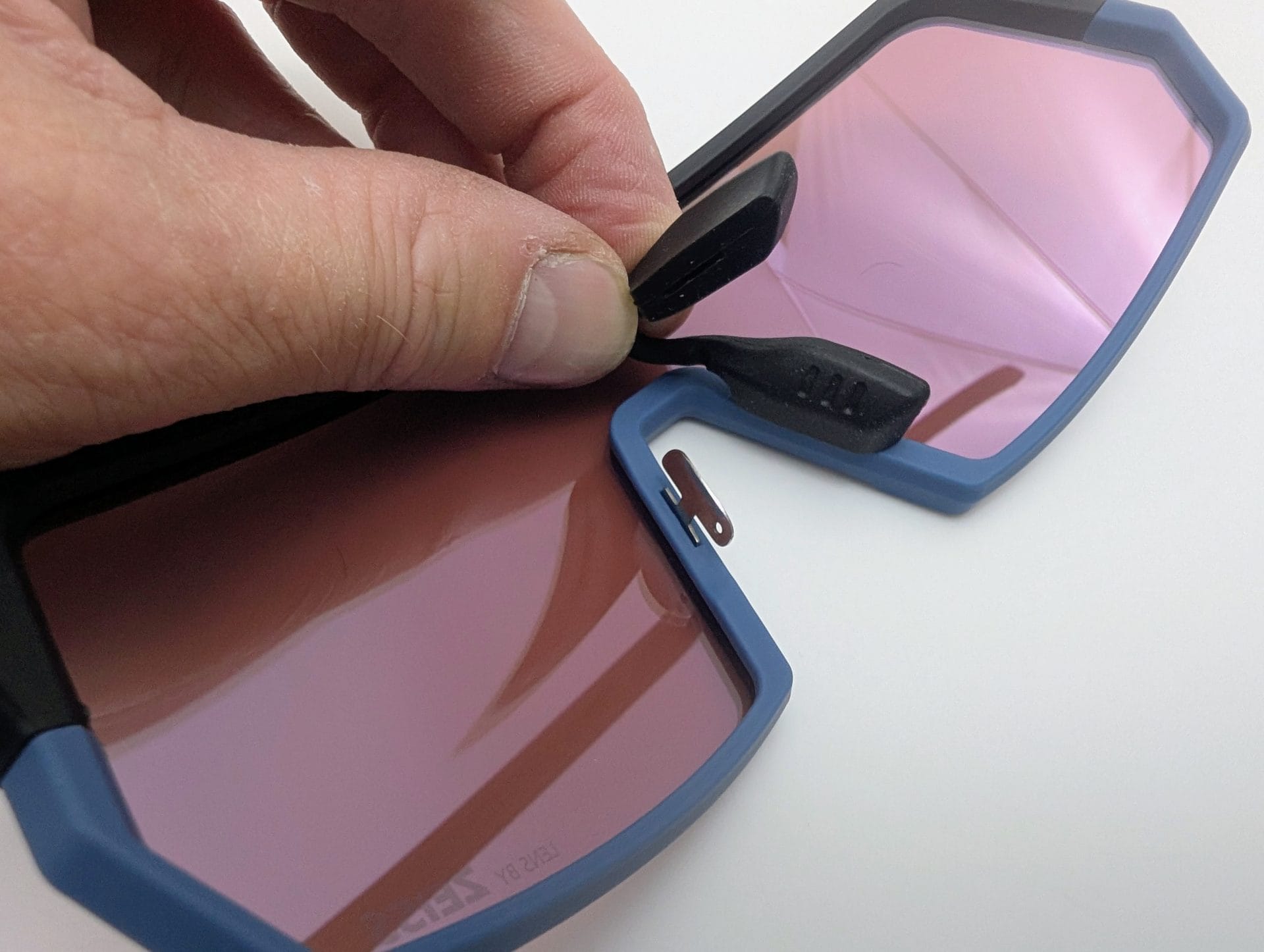 Outdoor Master Phoenix X Sports Sunglasses Demonstrating the adjustable nose piece on Outdoor Master Phoenix X performance sunglasses – black rubber nose pads being attached to the blue and black frame with pink reflective lenses.