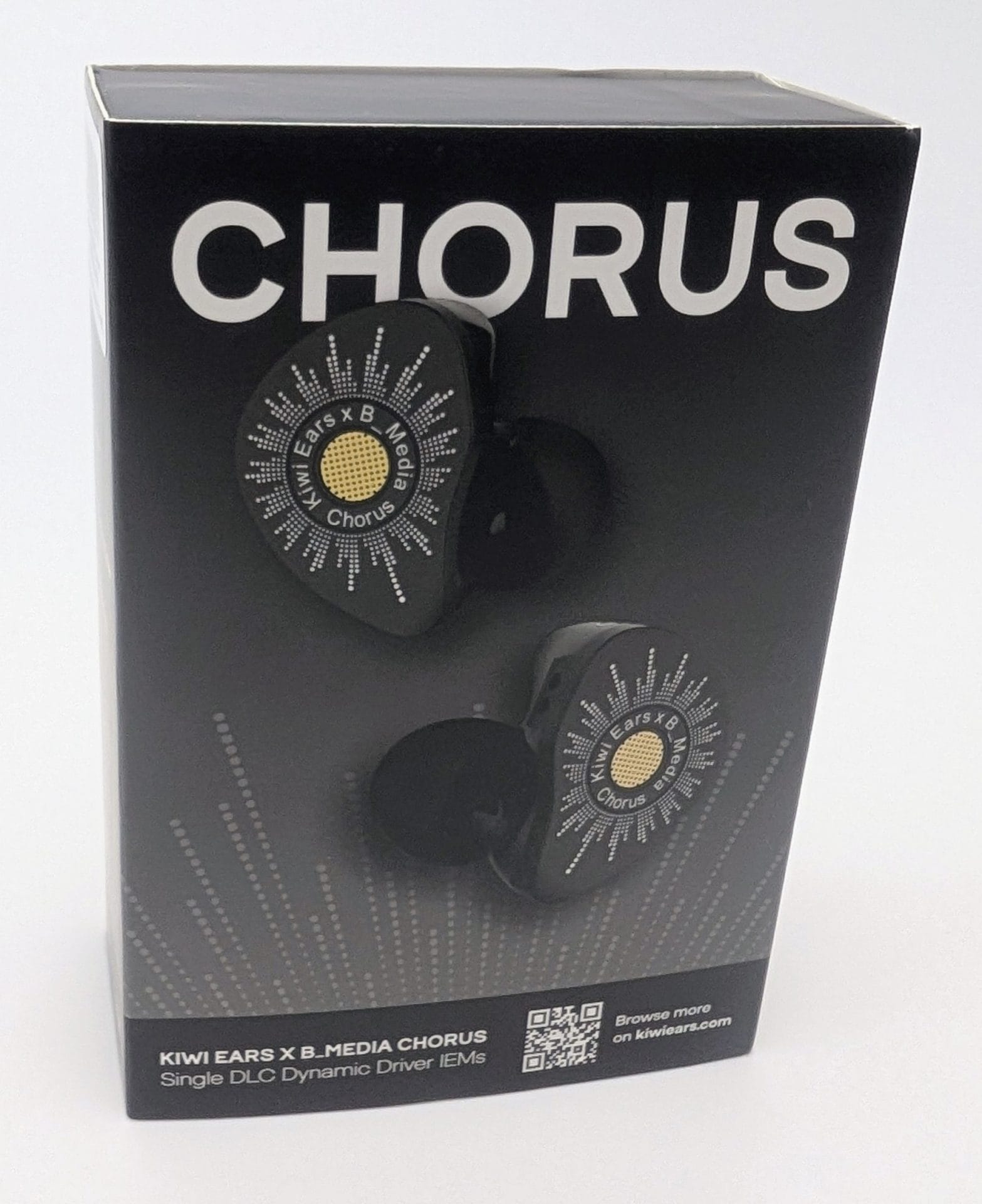 Kiwi Ears Chorus Black product box for Kiwi Ears x B_Media Chorus single DLC dynamic driver IEMs. Large white “CHORUS” text at the top; the front shows two black in-ear monitors with circular faceplates featuring white radial dotted patterns and a central gold mesh labeled “Kiwi Ears x B_Media Chorus”; bottom text reads “KIWI EARS X B_MEDIA CHORUS Single DLC Dynamic Driver IEMs” next to a QR code and “Browse more on kiwiears.com.