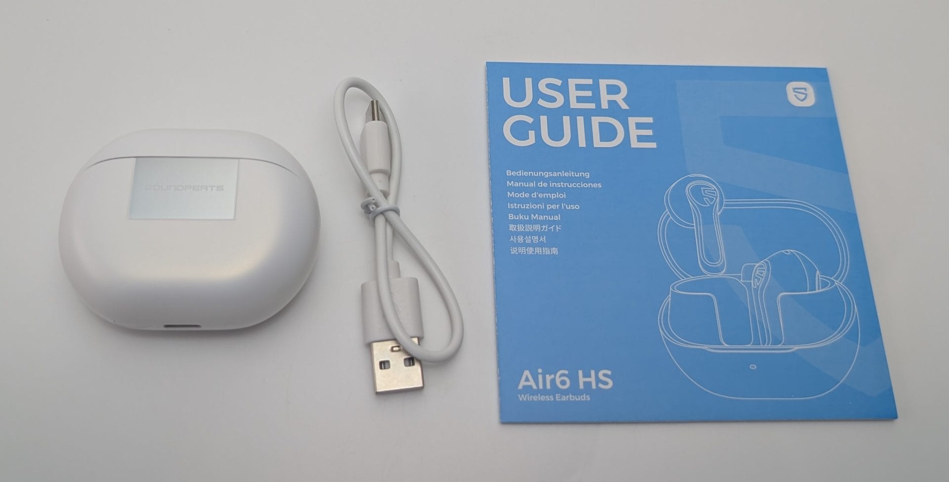 SoundPEATS Air6 HS White SoundPEATS Air6 HS wireless earbuds charging case (closed, with metallic logo plate), coiled white USB-A to USB-C charging cable, and blue multilingual user guide booklet showing an illustration of the open case with earbuds inside, labeled “Air6 HS Wireless Earbuds.”