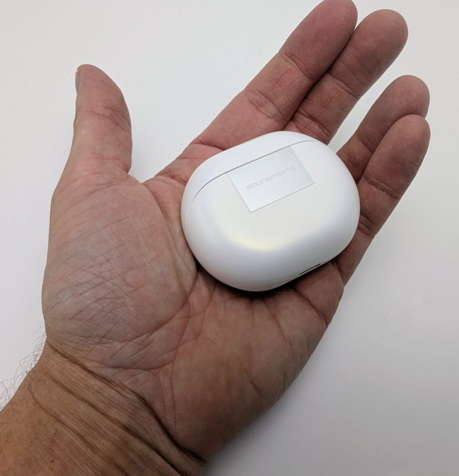 SoundPEATS Air6 HS A person’s open left hand holding a compact white SoundPEATS Air6 HS charging case, showing the silver logo plate with “SOUNDPEATS” text, against a plain white background.