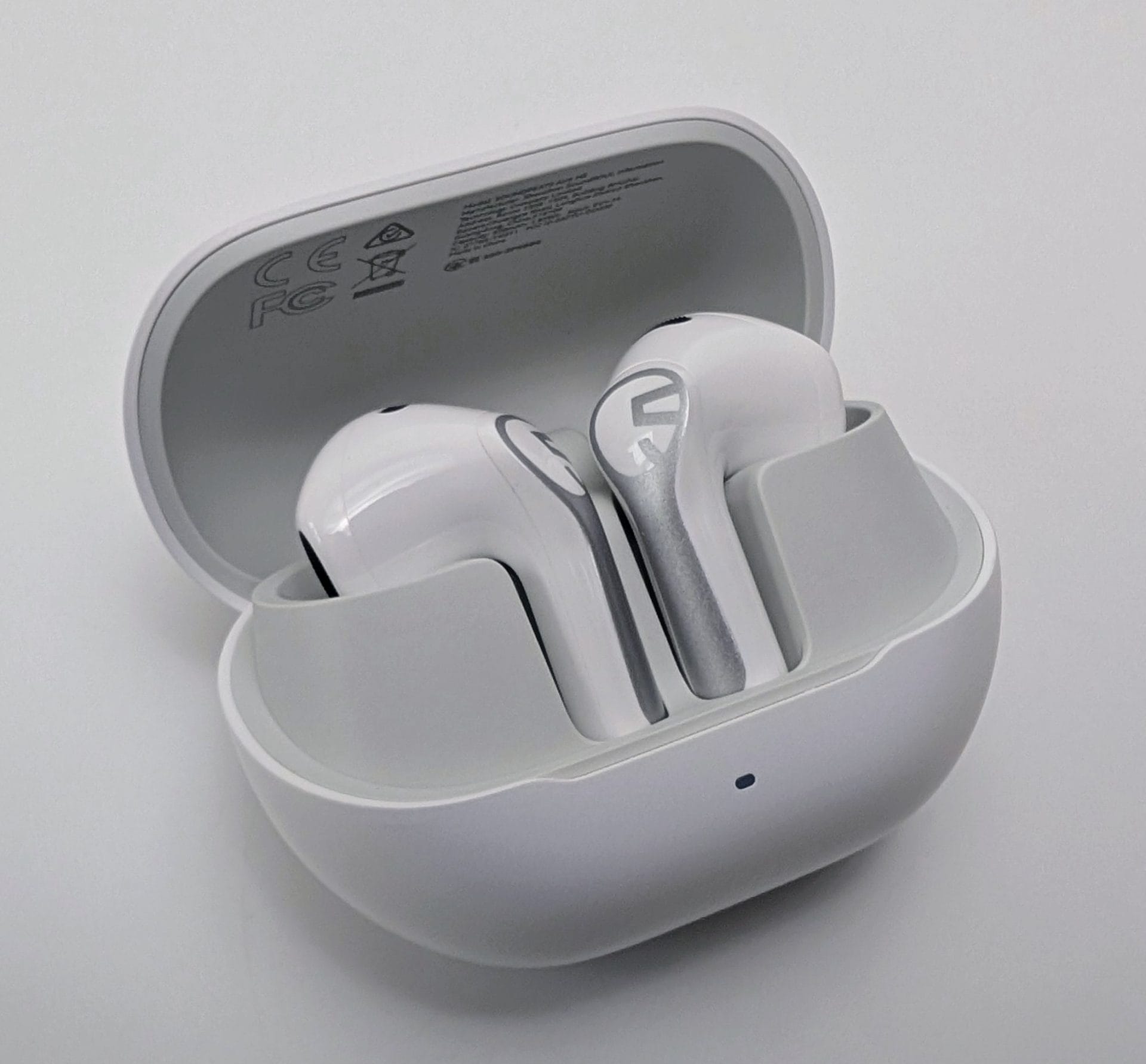 SoundPEATS Air6 HS Open white SoundPEATS Air6 HS charging case with both white earbuds seated inside, showing silver logos on the stems, regulatory markings (CE, FC) inside the lid, and a small LED indicator light on the front of the case.
