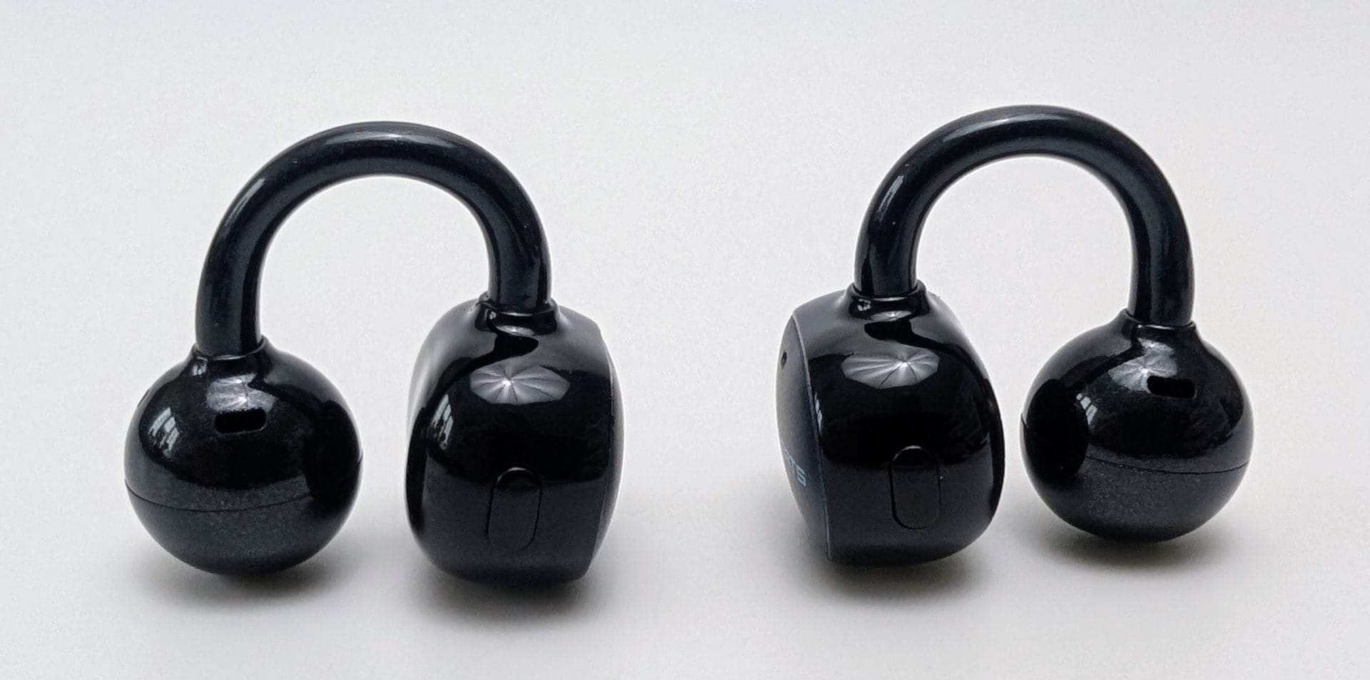 SoundPEATS UU2 Pair of glossy black SoundPEATS UU2 (POP Clip2) open-ear clip-on earbuds on a white background. Each earbud has a U-shaped hook connecting a spherical speaker housing to a compact control body with a physical button. The left earbud is shown with the sphere on the left and the body facing forward; the right earbud is flipped the other way, showing the opposite sides of the same design.